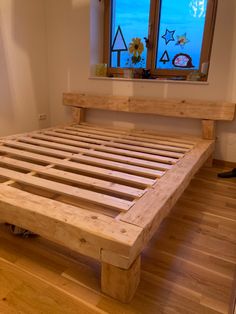 a wooden bed frame sitting on top of a hard wood floor next to a window