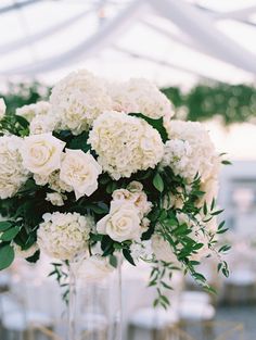 a vase filled with white flowers sitting on top of a table covered in greenery