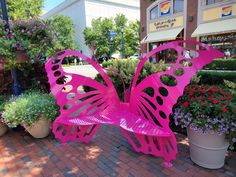 a pink butterfly sculpture sitting on top of a brick sidewalk next to potted plants