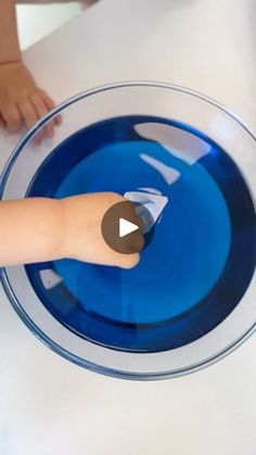 a toddler is playing with a blue bowl on a white table top and the child's hand is touching it