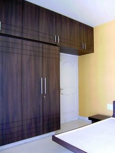 an empty bedroom with wooden cabinets and white sheets on the bed, in front of a yellow wall