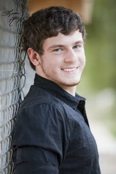 a young man leaning against a fence smiling at the camera with his hands on his hips