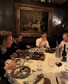 four men sitting at a dinner table with food and wine in front of their faces