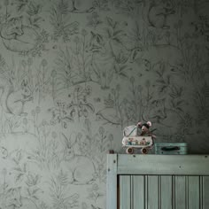 a teddy bear sitting on top of a dresser next to a wallpapered wall