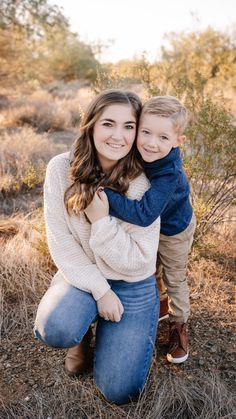 a woman holding a boy in her arms and smiling at the camera while sitting on the ground