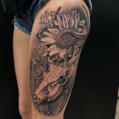 a black and white photo of a cow skull with sunflowers on it's thigh