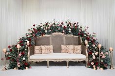 a white couch sitting under a floral covered arch with candles and flowers on the back