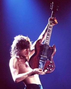 a shirtless man holding an electric guitar