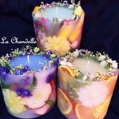 three candles with flowers and leaves on them sitting next to each other in front of a black background