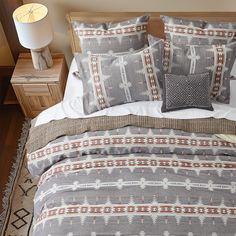 a bed with two pillows on top of it next to a night stand and lamp