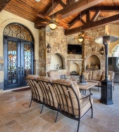 an outdoor living room with stone walls and wood ceilinging, large couches and fireplace