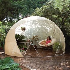 a woman sitting on a chair in a large white dome tent with trees around it