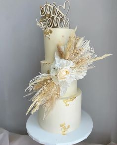 a three tiered wedding cake decorated with gold feathers and white flowers on a plate