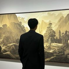 a man standing in front of a painting on display at an art gallery with mountains behind him