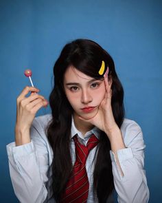 a woman in a tie holding a lollipop and looking at the camera with her hand near her face