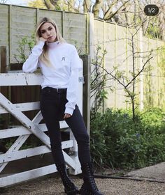 a woman leaning against a fence with her hand on her head and wearing black boots