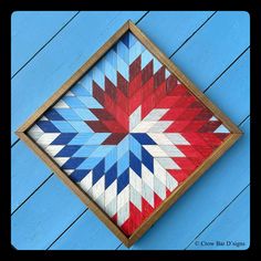 a red, white and blue quilt in a wooden frame on a blue wall with wood planks