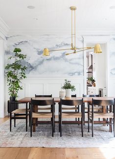 the dining room table and chairs are in front of a wall with clouds painted on it