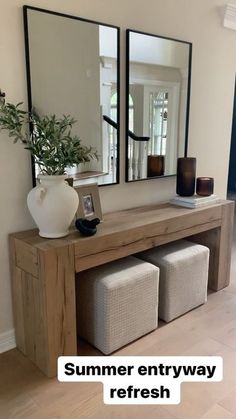 a large mirror sitting on top of a wooden table next to a vase and two stools