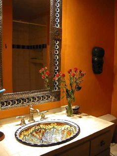 a bathroom with orange walls and white counter tops, decorated with flowers in vases