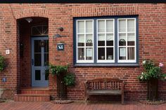 a wooden bench sitting in front of a brick building with two windows and potted plants