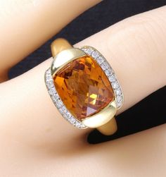 A wonderfully designed, luxurious 18k yellow gold natural bright golden citrine and diamond ring is ready to become your statement piece. The 5.50 carat citrine is stunning, measures 12x10mm antique cushion cut and set in a half bezel tension style mount. The 18 VS clarity G color diamonds, all perfectly matched, full cut round brilliant total .20 carats. Weighs 8.8 grams and is a size 7.5. Measures 17x14mm across the top, (25mm to an inch) and is marked 750. Excellent condition. Gold Cushion Cut Topaz Ring For Formal Occasions, Formal Gold Cushion Cut Topaz Ring, Gold Cushion Cut Topaz Ring, Luxury Amber Topaz Anniversary Ring, Luxury Amber Topaz Ring For Anniversary, Antique Cushion Cut, Antique Cushion, Half Bezel, Estate Ring