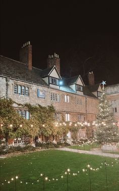 a christmas tree is lit up in front of an old building with lights on it