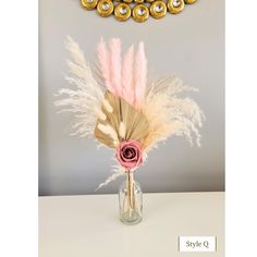 a vase with flowers and feathers in front of a gold necklace hanging on the wall