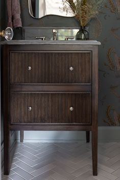 a bathroom vanity with two drawers and a mirror on the wall above it, in front of a patterned wallpapered wall