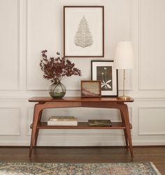 a wooden table topped with a vase filled with flowers next to a lamp and framed pictures