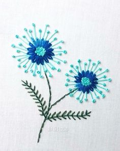 two blue flowers with green stems on a white background, one is embroidered and the other is beaded