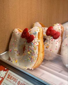 two donuts with white frosting and sprinkles are on display in a case