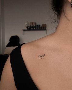 the back of a woman's shoulder with a small heart tattoo on her left side