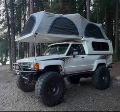 a white truck with a camper on the back parked in front of some trees