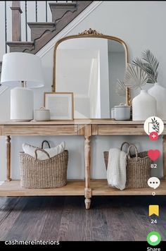 a wooden table topped with baskets under a stair case next to a mirror and lamp