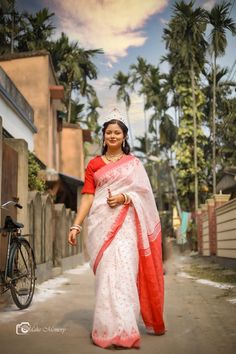 a woman in a red and white sari is walking down the street with her bike