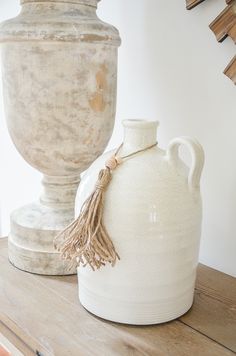 a white vase sitting on top of a wooden table next to a cement urn