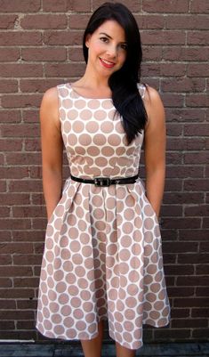 a woman standing in front of a brick wall wearing a dress with circles on it