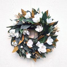 a wreath with white flowers and green leaves hanging on a door frame against a wall