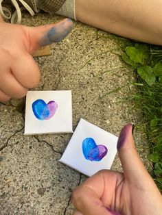 two hands holding small pieces of paper with hearts painted on them