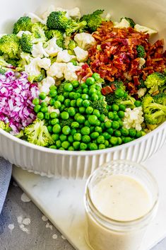 a bowl filled with peas, broccoli and other vegetables next to a bottle of ranch dressing