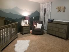 a baby's room with mountains painted on the wall and two cribs