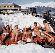 five people lounging on an inflatable mattress at the top of a ski slope