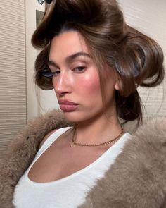 a woman with her hair in a bun is looking at the camera while wearing a fur coat