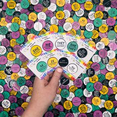 a hand holding three stickers in front of a pile of colorful buttons