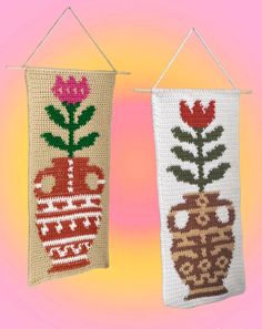 two crocheted wall hangings with flowers and vases on them, one has a pink background