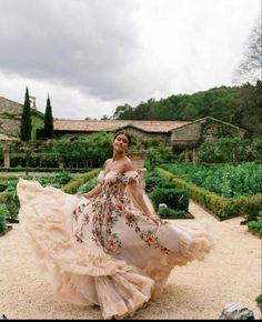 a woman in a long dress is walking through the garden with her hands on her hips