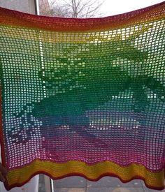 a colorful crocheted blanket hanging on a window sill in front of a building