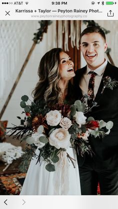 a man and woman standing next to each other in front of a wall with flowers