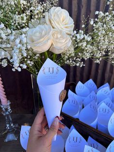 a person holding up a paper cone with flowers in it and place cards on the table